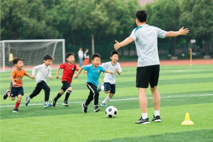 一位体育老师正在指导一群孩子进行足球训练，孩子们充满活力地奔跑在绿茵场上